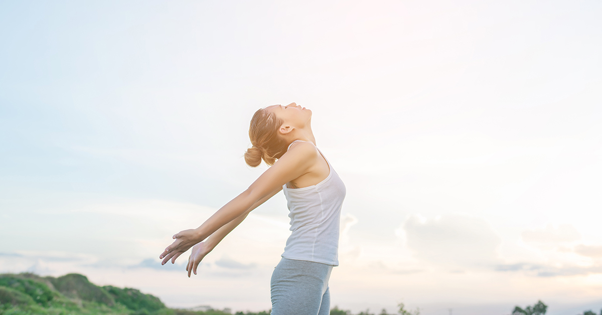 Young beautiful woman raising hands with beautiful view at meado