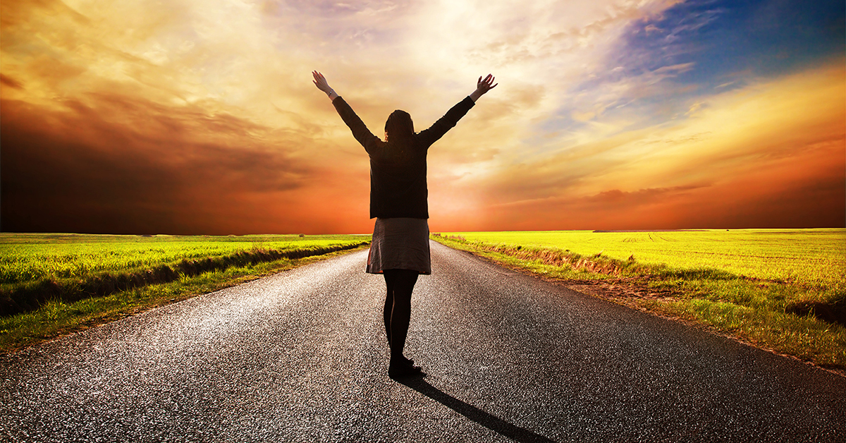 Happy woman standing on long road at sunset