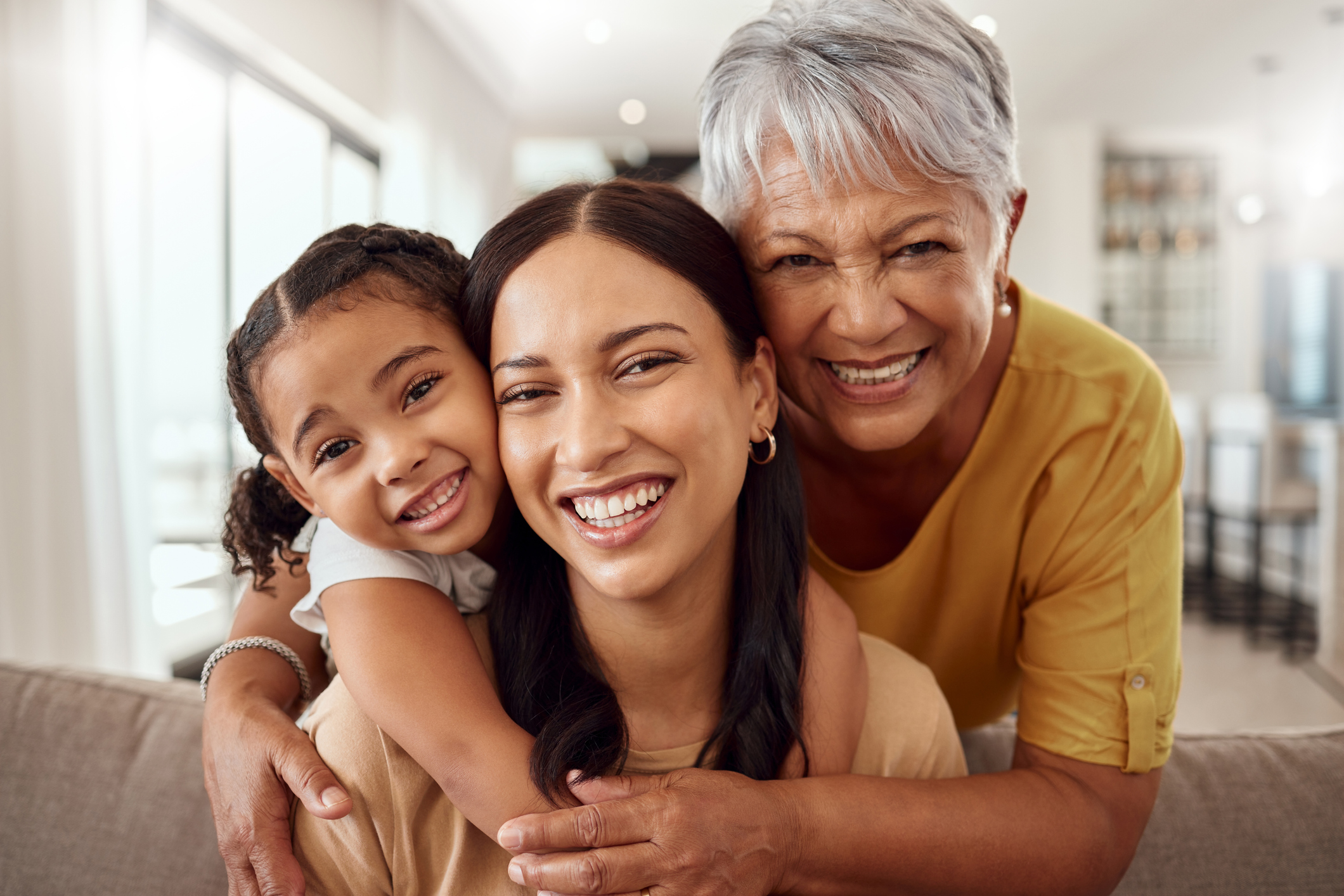 Child, mother and grandmother portrait while at home on sofa with smile, love and support sharing hug for generation of senior, woman and child. Portrait of brazil girls happy on mothers day together